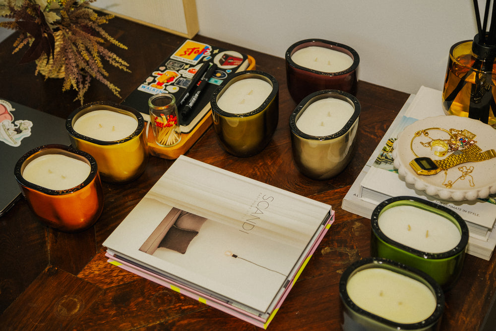 Candles of various sizes and colors on a wooden surface with a book and decorative items.